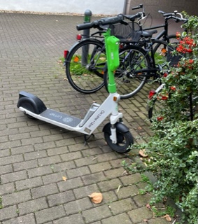 Ein abgestellter E-Scooter steht quer über einen Gehweg.