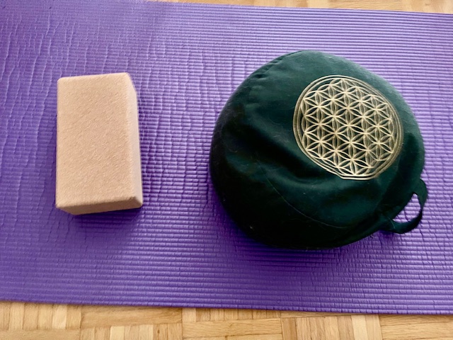 Auf einer Yogamatte liegen ein Meditationskissen und ein Yoga-Block aus Kork.