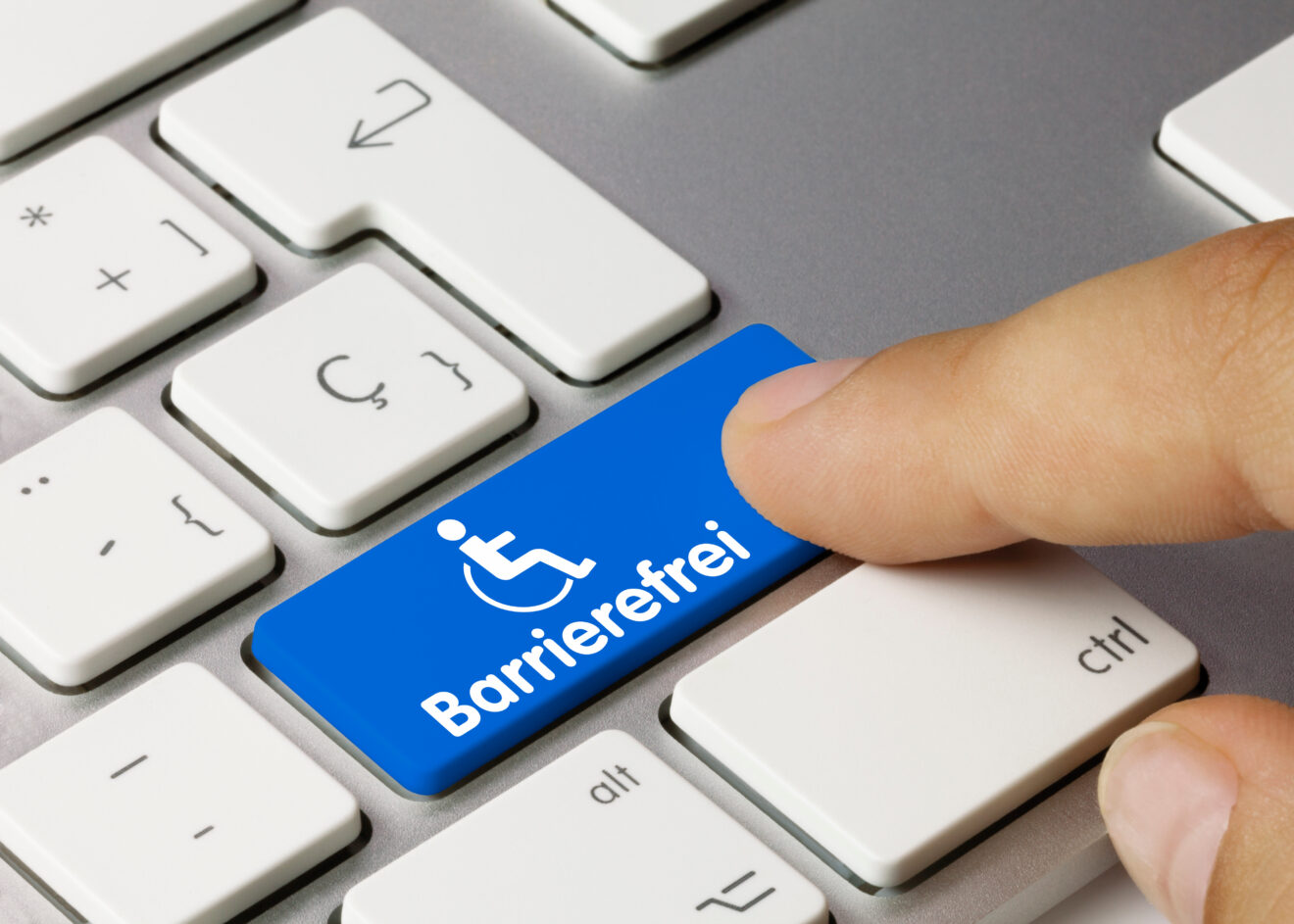 Das Bild zeigt die untere rechte Ecke einer PC-Tastatur, auf der ein Finger eine blau unterlegte Taste drückt. Auf der Taste steht in weißen Buchstaben das Wort barrierefrei, darüber sieht man das Piktogramm einer Rollstuhl-nutzenden Person wie auf einem Behinderenparkplatz.