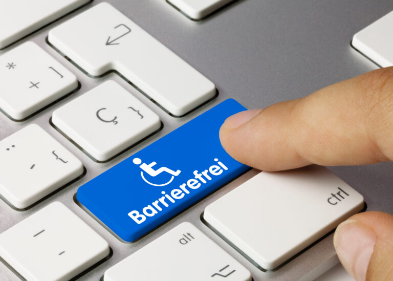 Das Bild zeigt die untere rechte Ecke einer PC-Tastatur, auf der ein Finger eine blau unterlegte Taste drückt. Auf der Taste steht in weißen Buchstaben das Wort barrierefrei, darüber sieht man das Piktogramm einer Rollstuhl-nutzenden Person wie auf einem Behinderenparkplatz.